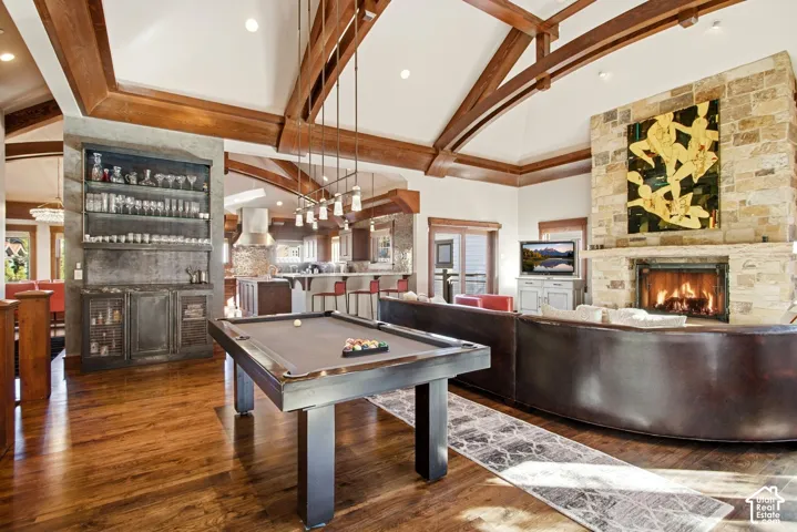 Vaulted ceiling with decorative wood beams, floor-to-ceiling stone fireplace, wood-finish flooring, and built-in glass-front cabinetry