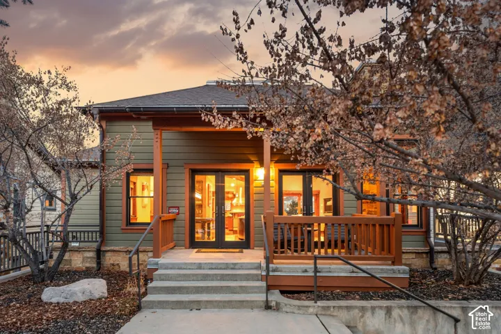 Exterior facade featuring horizontal lap siding, stone foundation, covered porch with wood railings, and glass-paneled double doors
