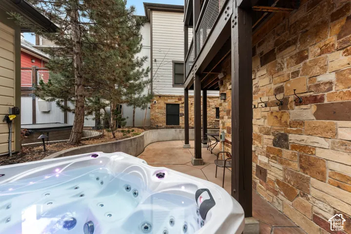 Covered stone patio featuring a built-in spa, structural wood-frame supports, and a natural stone exterior wall with mounted hardware