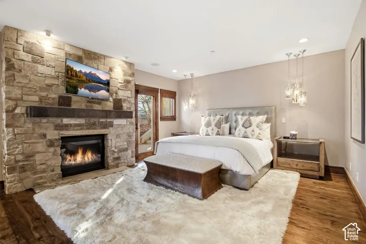 Full-height stacked stone fireplace surround with a dark timber mantel, recessed ceiling lighting, wood-finish flooring, and multi-light glass pendant fixtures