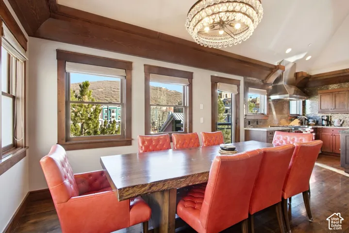 Dining area featuring vaulted ceilings with crown molding, thick wood window casing, drum chandelier with crystal detailing, and wood-finish flooring