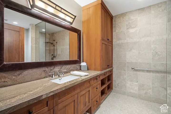 Custom wood cabinetry featuring integrated storage, stone-surfaced countertop with an inset sink, large-format tiled shower walls, and a recessed medicine cabinet lighting fixture