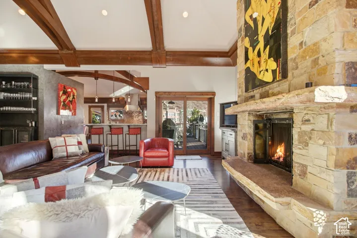 Vaulted ceiling featuring exposed wood beams, floor-to-ceiling stone fireplace with a thick slab hearth, wood-finish flooring, and sliding glass doors