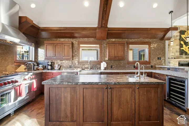 Kitchen featuring custom wood cabinetry, a central island with stone-surface countertop, high-end stainless steel appliances, decorative tile backsplash, and vaulted ceilings with exposed wood beams