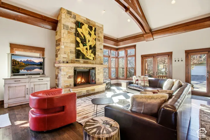 Vaulted ceilings featuring exposed timber beams, full-height stone fireplace, wood-finish flooring, and large paneled windows with wood trim