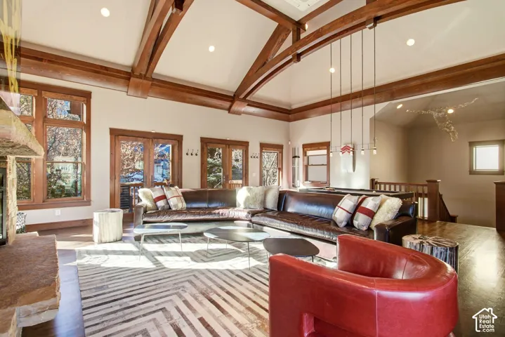 Vaulted ceiling featuring exposed wood-beam construction, natural stone fireplace, recessed lighting, and multiple wood-encased glass doors