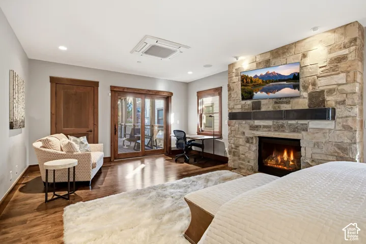 Floor-to-ceiling natural stone fireplace with a built-in mantel, recessed ceiling lighting, sliding glass door with wood trim, wood-finish flooring, and solid wood interior door