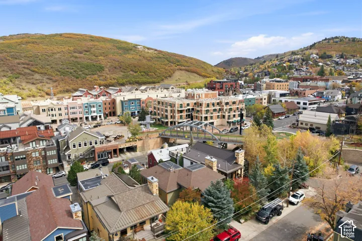 Aerial perspective of a mountain town setting featuring mixed-use architecture, prominent arched pedestrian bridge, stone and metal roofing accents, and rolling hillside terrain