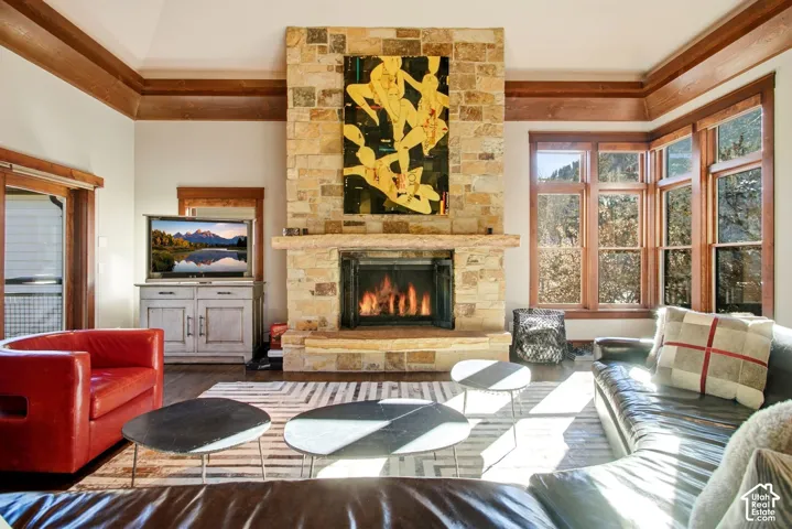 Full-height natural stone fireplace with a thick stone mantel, tray ceiling with dark-finish wood crown molding, and large-pane windows with matching wood trim