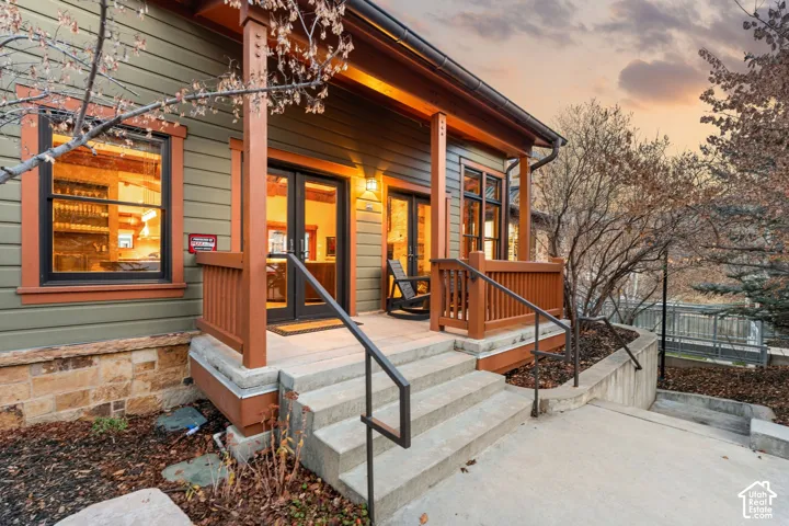 Exterior featuring horizontal siding, stone masonry base, covered porch with wood-finish railings, and glass-paneled double doors