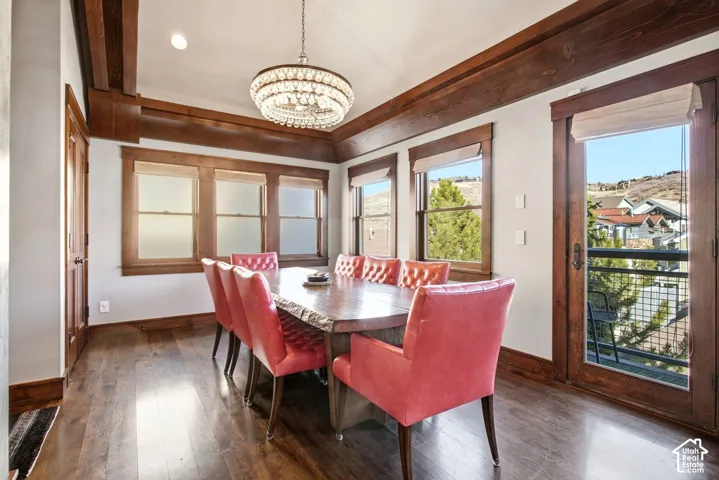 Dining area featuring wood-finish flooring, stained wood crown molding, a multi-tiered crystal chandelier, expansive windows, and a glass-paneled exterior door