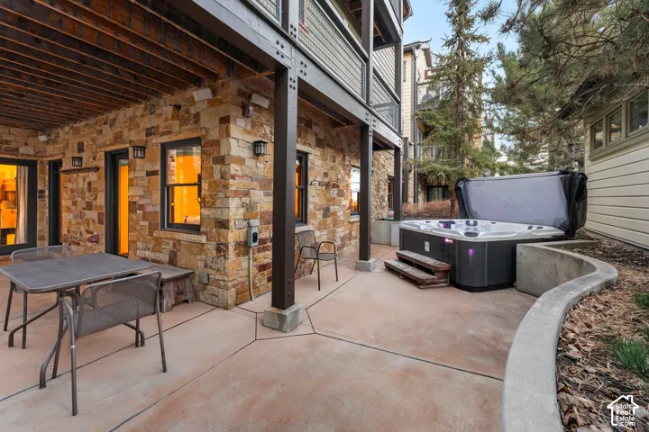 Covered patio featuring stacked stone masonry, concrete hardscaping, structural steel support columns, and an integrated hot tub with tiered steps