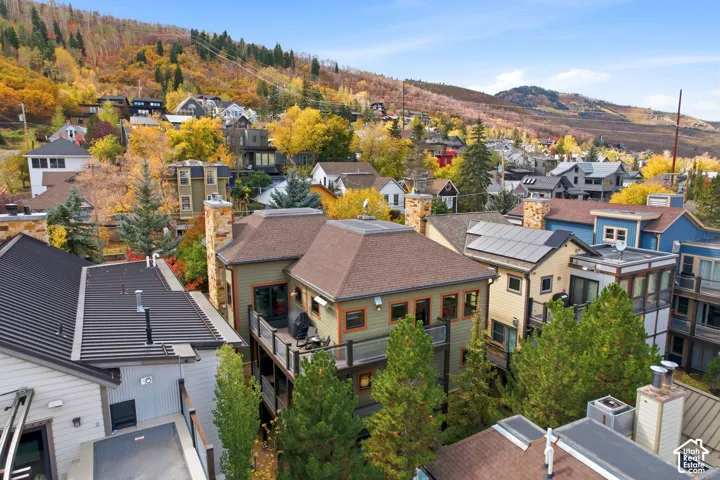 Multi-level residence featuring shingle roofing, dual stone chimneys, elevated balconies with metal and glass railings, and roof-mounted solar panels set against a mountainous backdrop