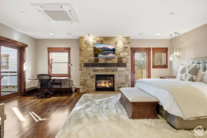 Floor-to-ceiling stone fireplace with a thick timber mantel, wood-finish flooring, recessed ceiling lighting, and rich wood-trimmed window and door casings