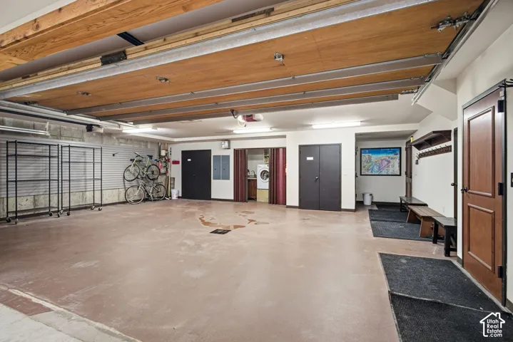 Multi-car garage featuring a smooth-finish floor, overhead door, fluorescent lighting, built-in mudroom bench with wall-mounted coat hooks, and a dedicated laundry alcove