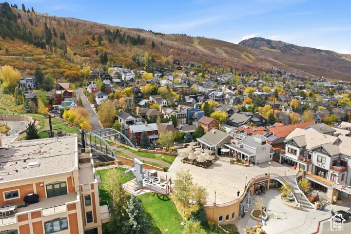 Aerial perspective of a multi-level brick and masonry property featuring an expansive stone-paved plaza, integrated staircases, manicured lawn areas, and proximity to mountain terrain