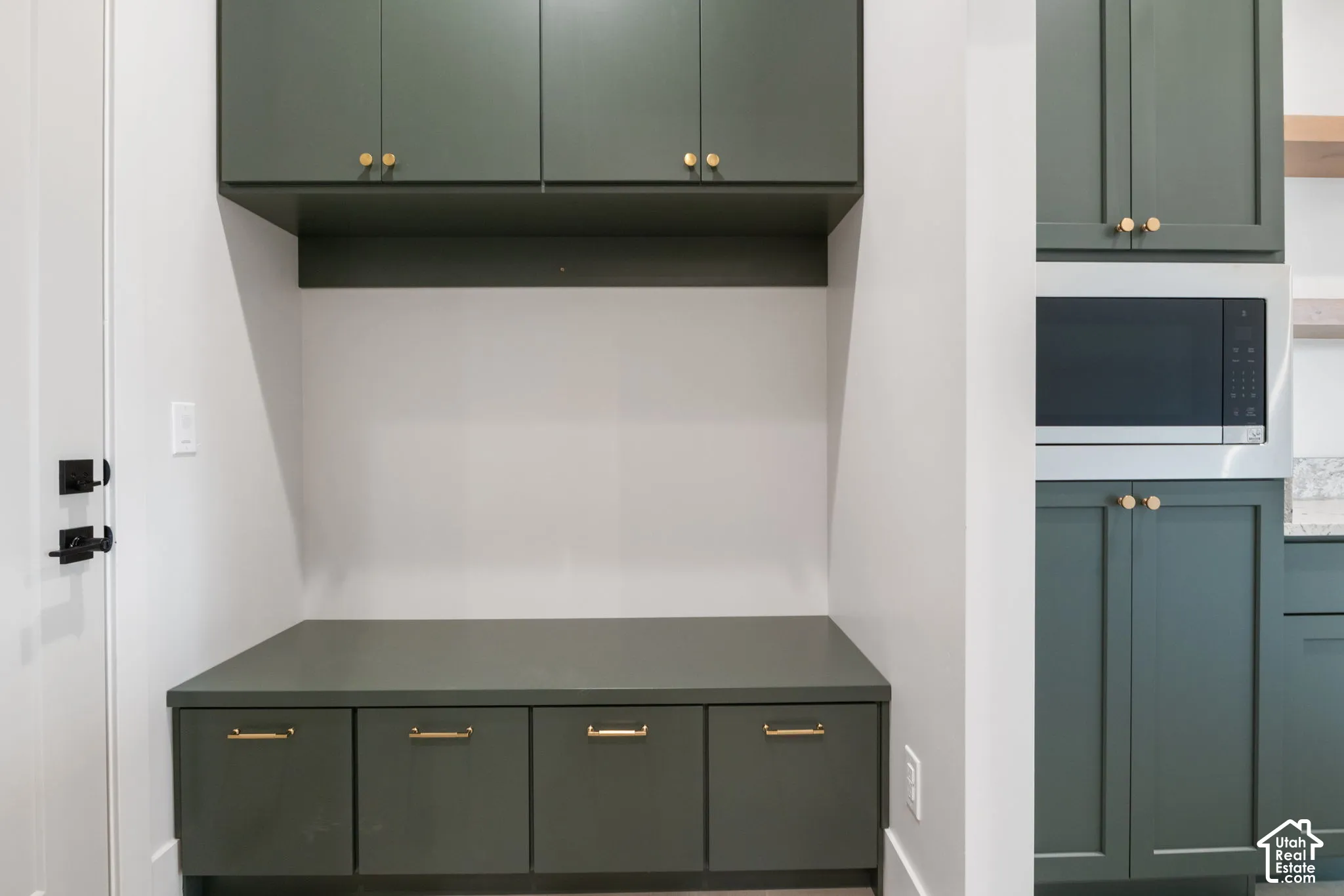 Custom built-in cabinetry featuring green flat-panel doors, integrated microwave, brass-tone hardware, and an expansive storage bench