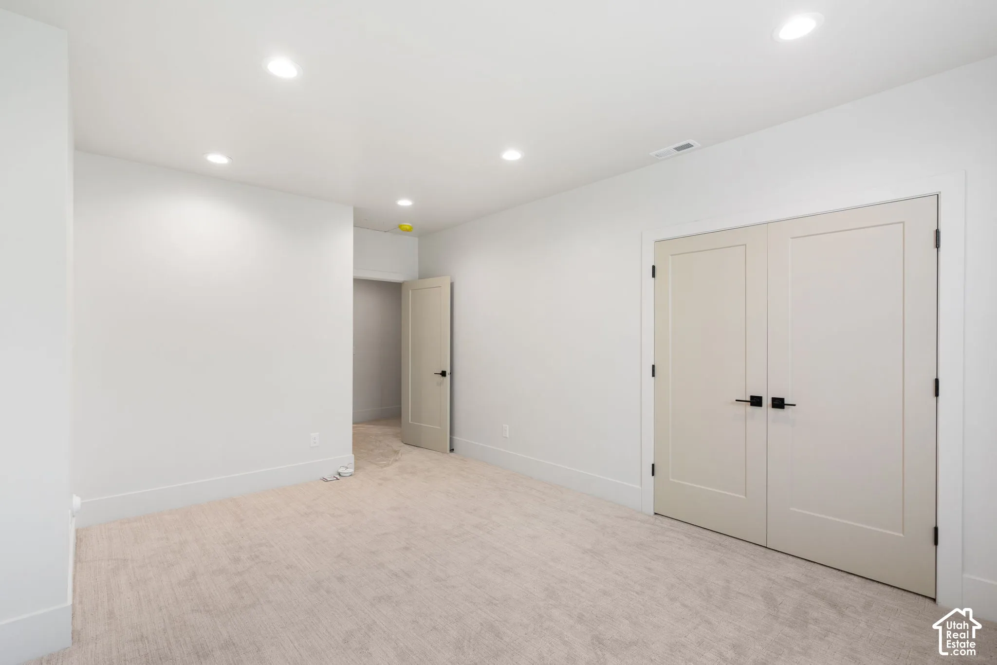 Neutral-toned interior space featuring recessed ceiling lighting, light-colored carpeting, and double doors with matte black hardware