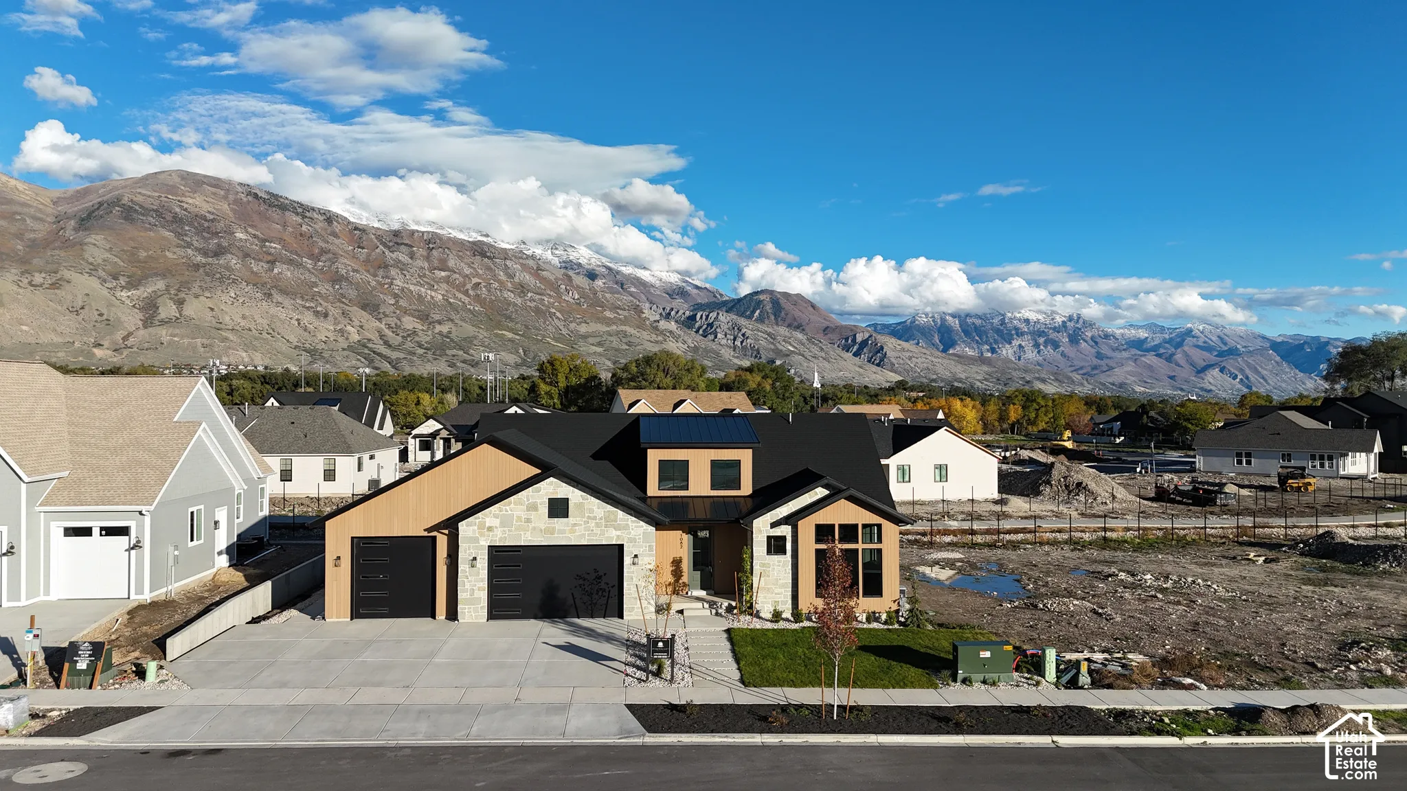 Contemporary exterior featuring a stone and wood-panel facade, multi-gabled roofline, expansive windows, and a three-car garage set against a prominent mountain backdrop