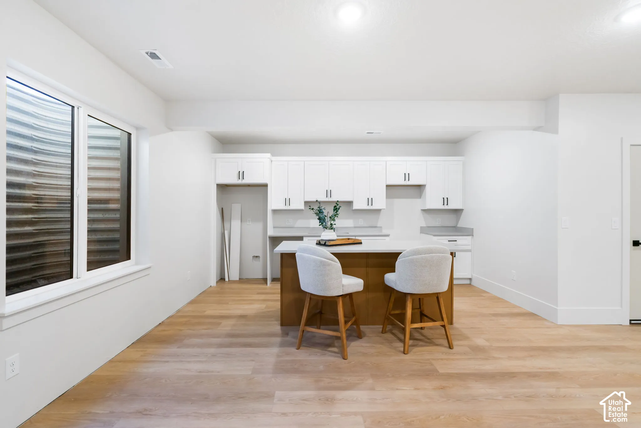 Kitchen featuring white shaker-style cabinetry, wood-finish flooring, a central island with a solid-surface countertop, and recessed ceiling lighting