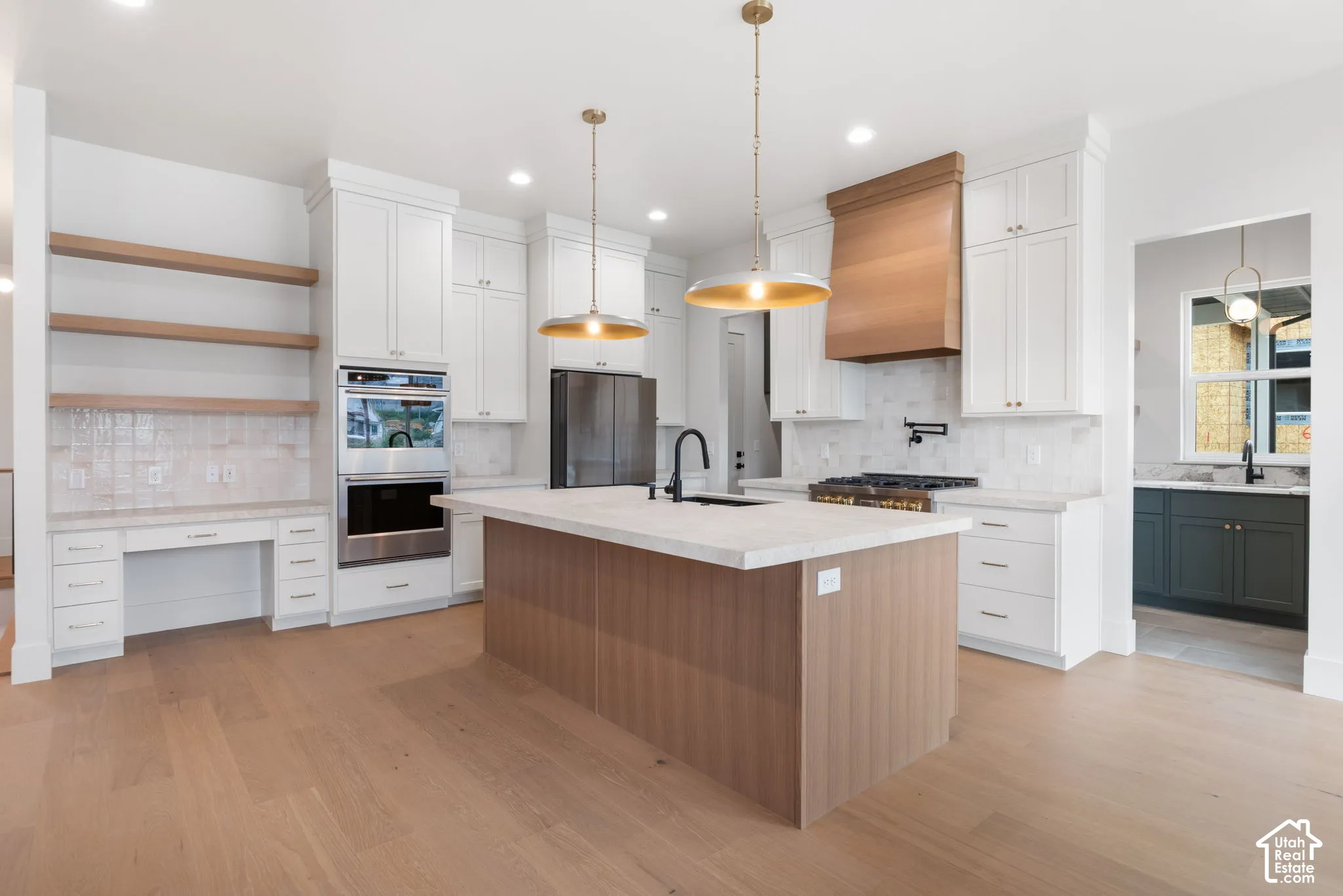 Kitchen featuring white shaker cabinetry, wood-finish center island, quartz countertops, stainless steel double wall oven, and built-in wood shelving