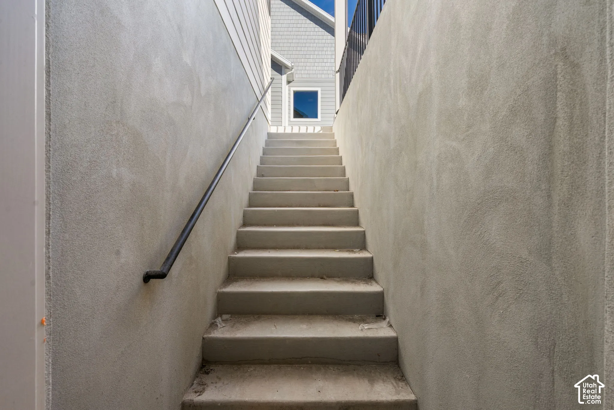 Exterior staircase featuring smooth stucco side walls, concrete steps, and a black metal handrail