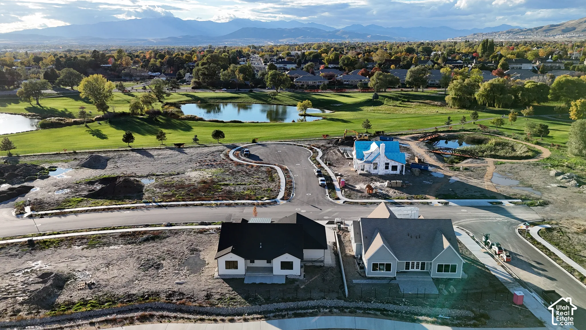 Aerial perspective of a residential development featuring custom single-family homes, paved cul-de-sacs, pond frontage, and mountain range backdrop