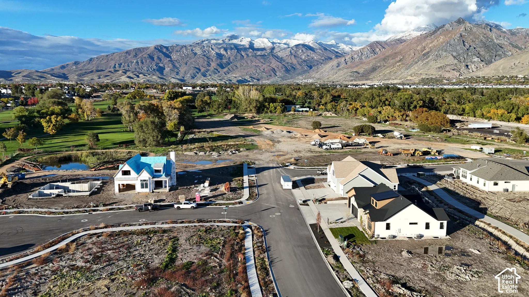 Aerial perspective of a developing residential community featuring mountain terrain, paved streets, sidewalks, and natural landscaping