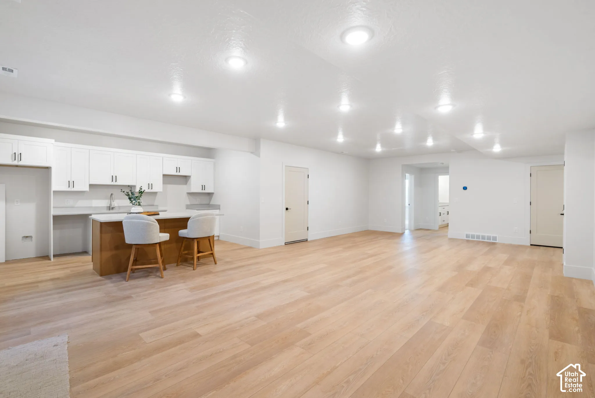 Open interior space featuring light-toned wood-finish flooring, recessed ceiling lighting, and a kitchenette with white cabinetry, a sink, and a central island
