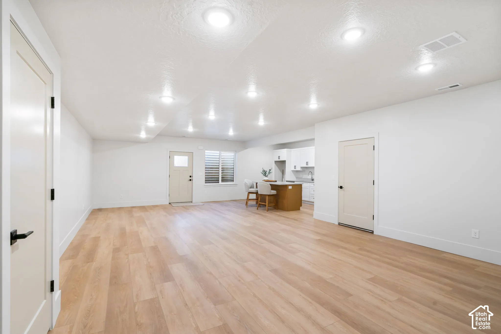 Open-concept area featuring wood-finish flooring, recessed lighting, and a kitchenette with white cabinetry and an island