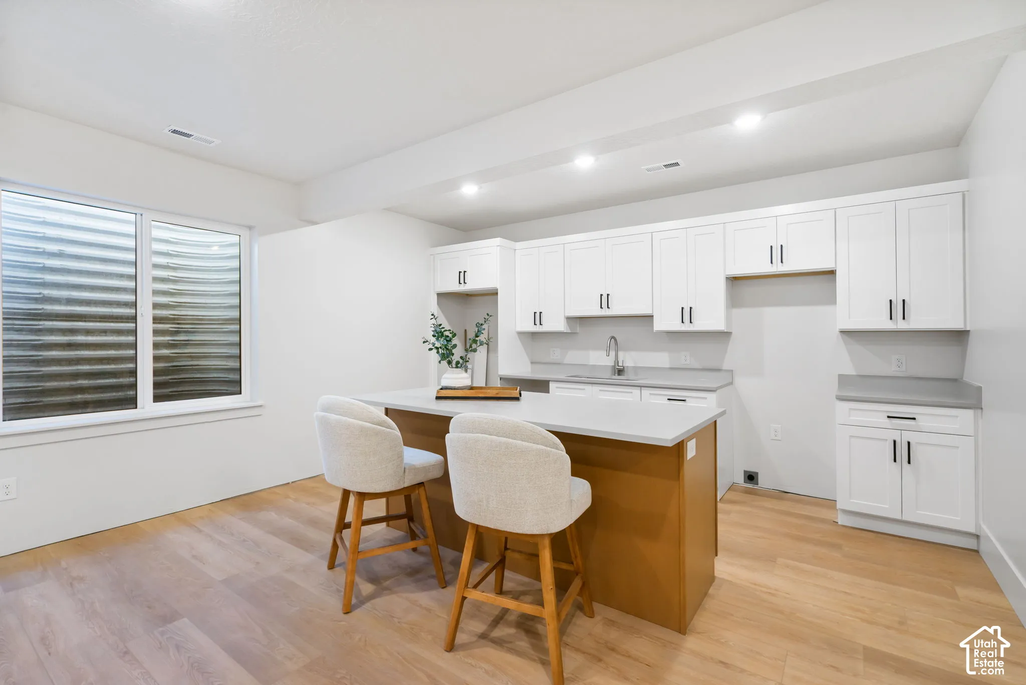 Kitchenette featuring white Shaker-style cabinetry, a central island with a wood-finish base, solid-surface countertops, recessed lighting, and wood-finish flooring