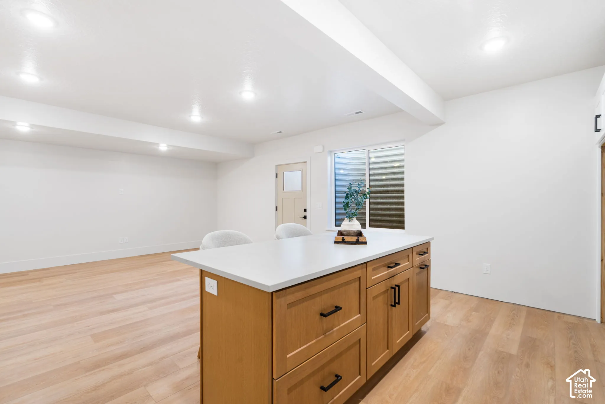 Center island featuring shaker-style cabinetry, matte black hardware, and a solid-surface countertop, complemented by recessed ceiling lighting and wood-finish flooring