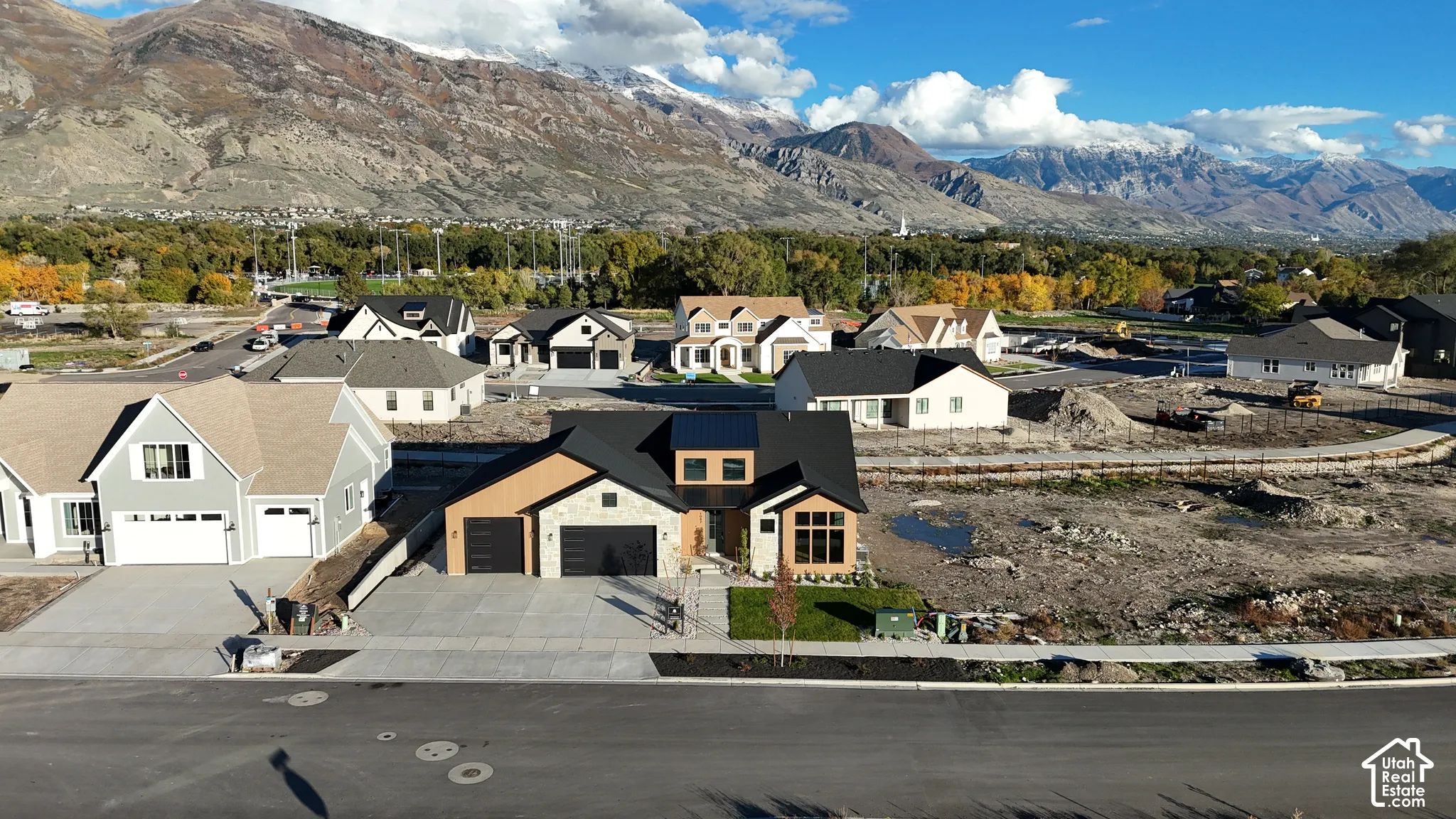 Contemporary residence featuring stone and wood-tone exterior siding, a multi-car garage, steep-pitch rooflines, and prominent mountain backdrops