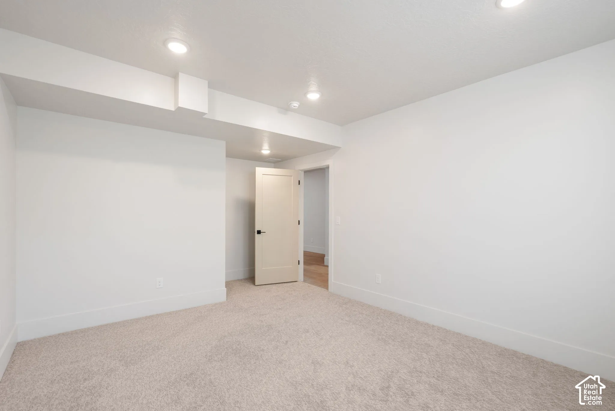 Neutral-toned wall-to-wall carpeting, recessed ceiling lighting, and a single-panel interior door with matte black hardware