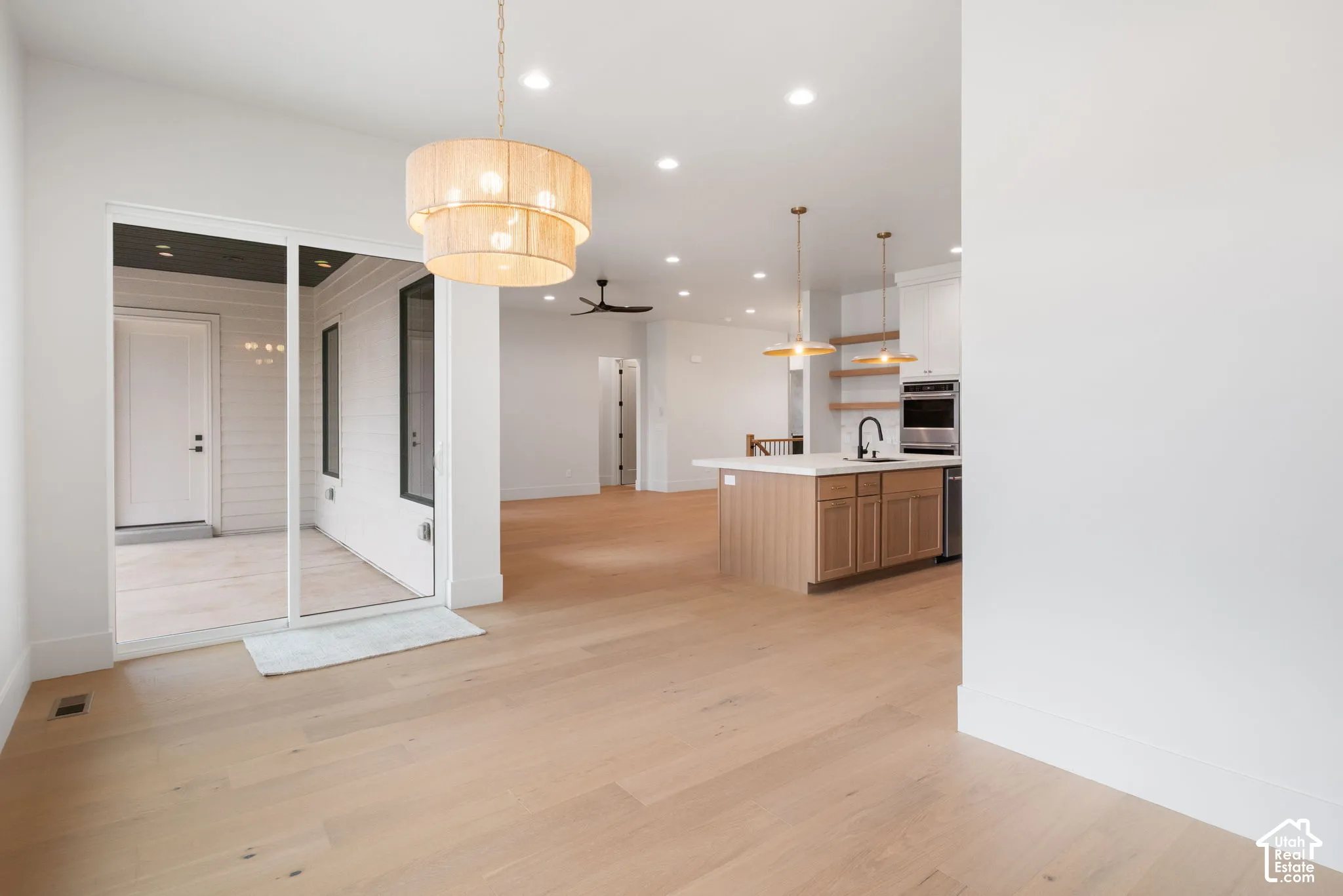 Open-concept area featuring light-tone wood-finish flooring, recessed lighting, a kitchen island with stone-surface countertops, tiered drum pendant lighting, and a large sliding glass door