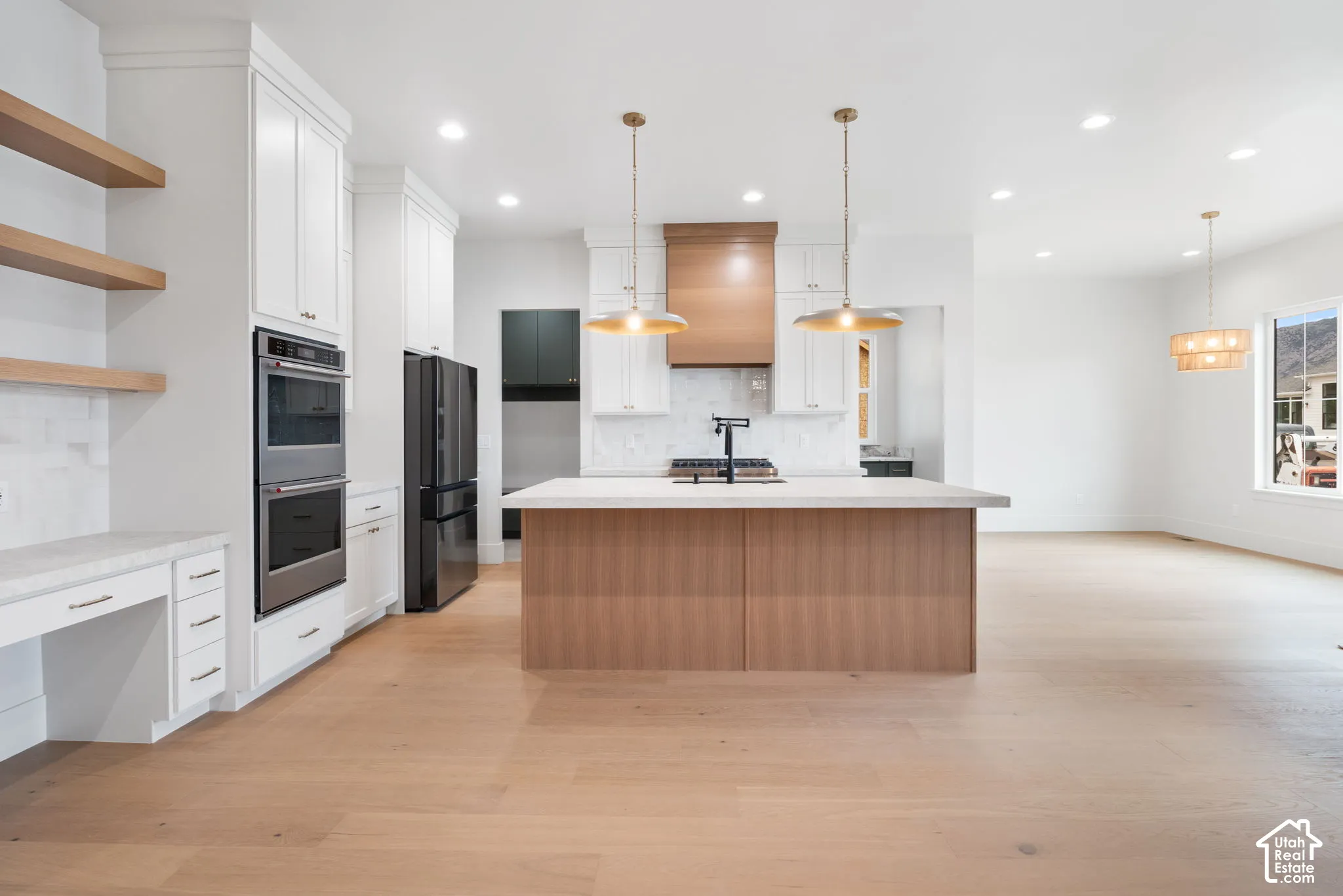 Kitchen featuring white shaker-style cabinetry, wood-finish flooring, a central island with a stone-top surface, dual wall ovens, and custom wood shelving