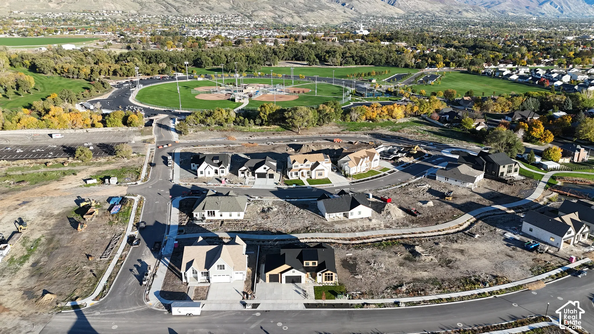 Aerial perspective of a residential development featuring paved street infrastructure, concrete driveways, multi-pitched rooflines, and mountain scenery