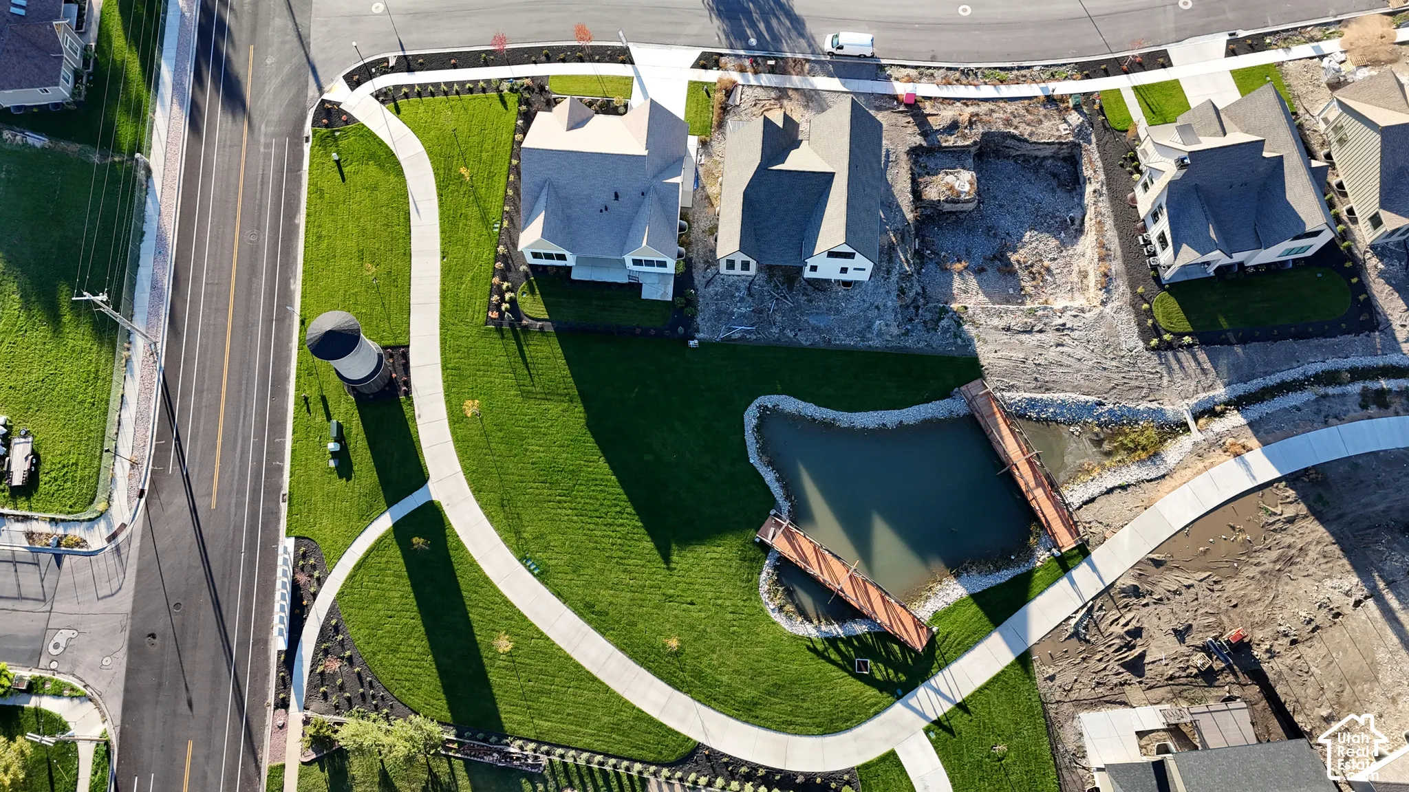 Aerial view featuring a pond, pedestrian bridge, expansive manicured lawn, and concrete walkways