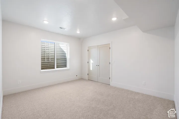 Neutral-toned interior space featuring light carpeting, recessed lighting, double-door closet, and an egress window