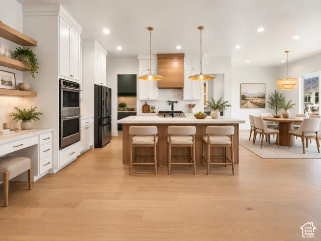 Kitchen featuring a central island with countertop seating, custom wood-finish hood range, built-in double ovens, white cabinetry, and wood-finish flooring
