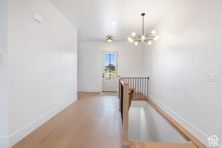 Interior space featuring light-tone wood-finish flooring, a multi-arm modern chandelier, a single-lite glass entry door with black muntins, and a staircase railing with wood handrails and vertical metal balusters