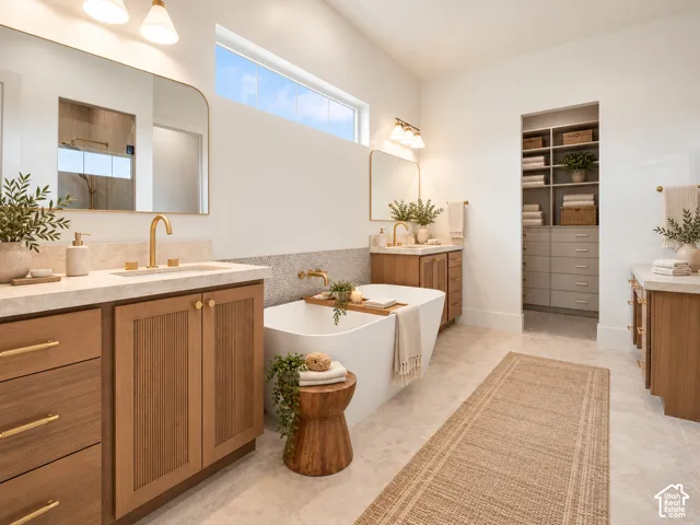 Freestanding soaking tub with wall-mounted brass hardware, dual wood-tone vanities featuring stone-finish countertops, and built-in walk-in closet shelving