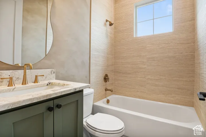 Bathroom featuring a stone-top vanity with brass hardware, wavy-edged wall mirror, textured tile walls, tub-shower combination, and matte brass fixtures
