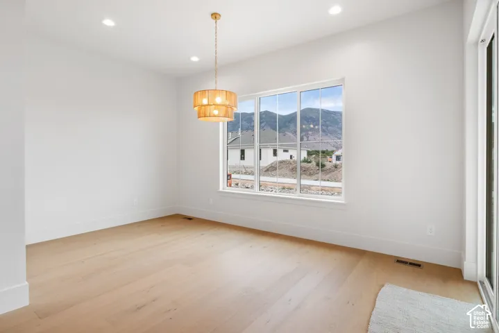 Interior space featuring light-tone wood-finish flooring, recessed lighting, a tiered drum pendant light fixture, and a large window showcasing mountain scenery