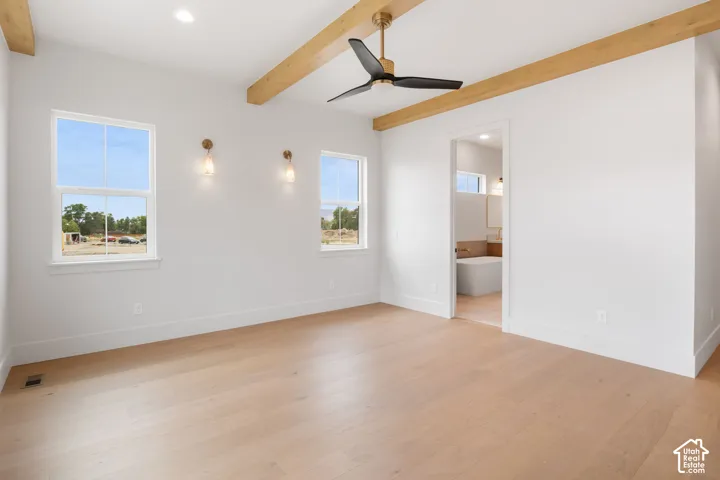 Neutral-toned room featuring light wood-finish flooring, exposed wooden ceiling beams, a matte black three-blade ceiling fan, and two glass wall-mounted light fixtures