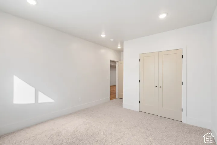 Neutral-toned interior room featuring recessed ceiling lighting, light-colored wall-to-wall carpeting, and double-panel closet doors with matte black hardware