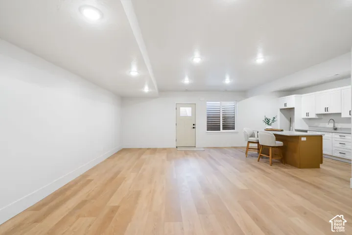 Open-concept interior featuring wood-finish flooring, recessed lighting, and a kitchenette with white cabinetry, a central island, and an undermount sink