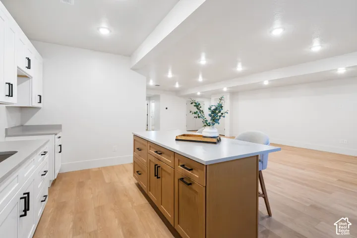 Kitchen area featuring white shaker-style cabinetry, wood-finish kitchen island with matte black hardware, stone-composite countertops, and recessed ceiling lighting