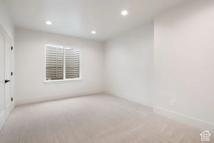 Neutral-toned interior space featuring wall-to-wall carpeting, recessed ceiling lighting, and an egress window with a corrugated metal window well