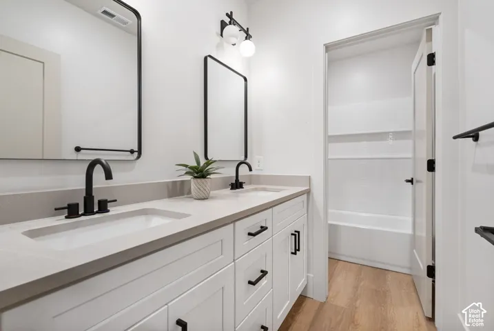Dual-sink vanity with white cabinetry, light-toned countertop, matte black fixtures, rectangular mirrors, and wood-finish flooring